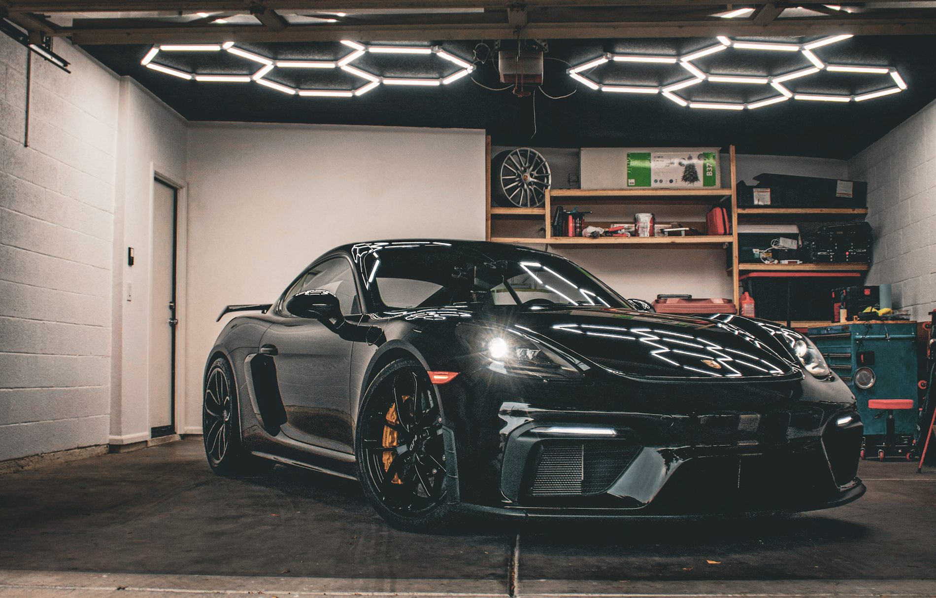 A black Porsche 718 GT4 parked under hexagonal garage lighting during a detail