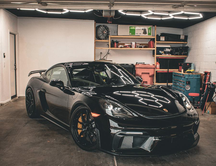 Black Porsche 718 Cayman GT4 under hexagonal garage lights