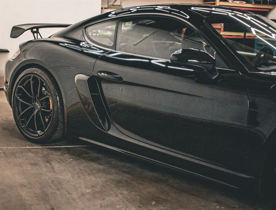 Black Porsche 718 Cayman GT4 side profile with a wet-look finish