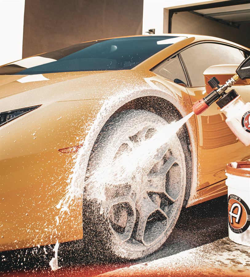 Thick foam being sprayed onto the forged wheel of an orange Lamborghini Huracán