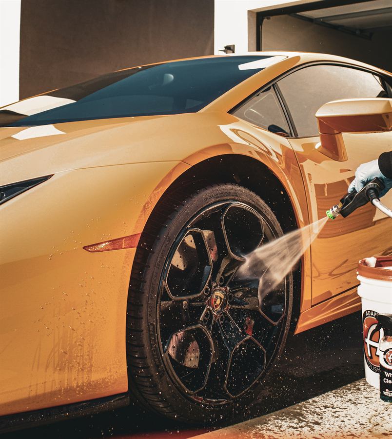 Pressure washer rinsing the wheel of an orange Lamborghini Huracán