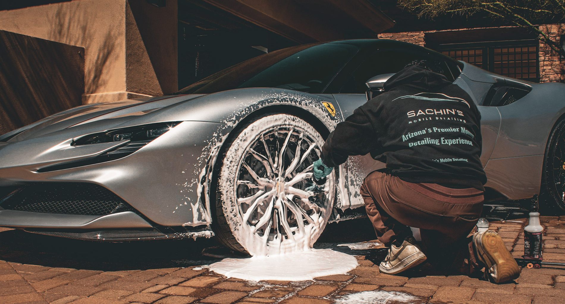 Sachin, in a branded hoodie, crouched down cleaning the wheel of a silver Ferrari